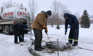 Three workers maintain a frozen septic system in the snow beside an Owens Septic Service truck.